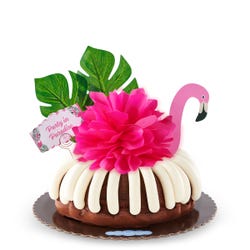 A bundt cake decorated with a pink flamingo with tropical leaves. It also includes a card that reads Party in Paradise.