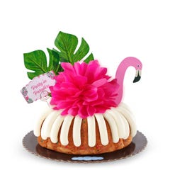 A Confetti bundt cake decorated with a pink flamingo with tropical leaves. It also includes a card that reads Party in Paradise. 