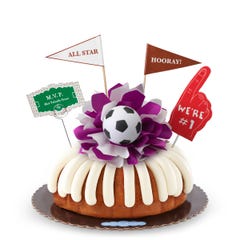 A Lemon bundt cake, decorated with a mini soccer ball on top of a purple and white bow in the center of the cake. 
