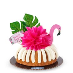 A Vanilla bundt cake decorated with a pink flamingo with tropical leaves. It also includes a card that reads Party in Paradise. 