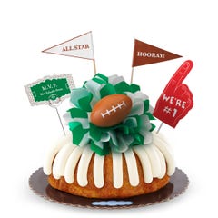 A White Chocolate Raspberry bundt cake with frosting, decorated with a mini football on top of a green and white bow in the center of the cake. The cake also contains a We're #1 foam finger, a flag that says All Star and a card that says MVP.